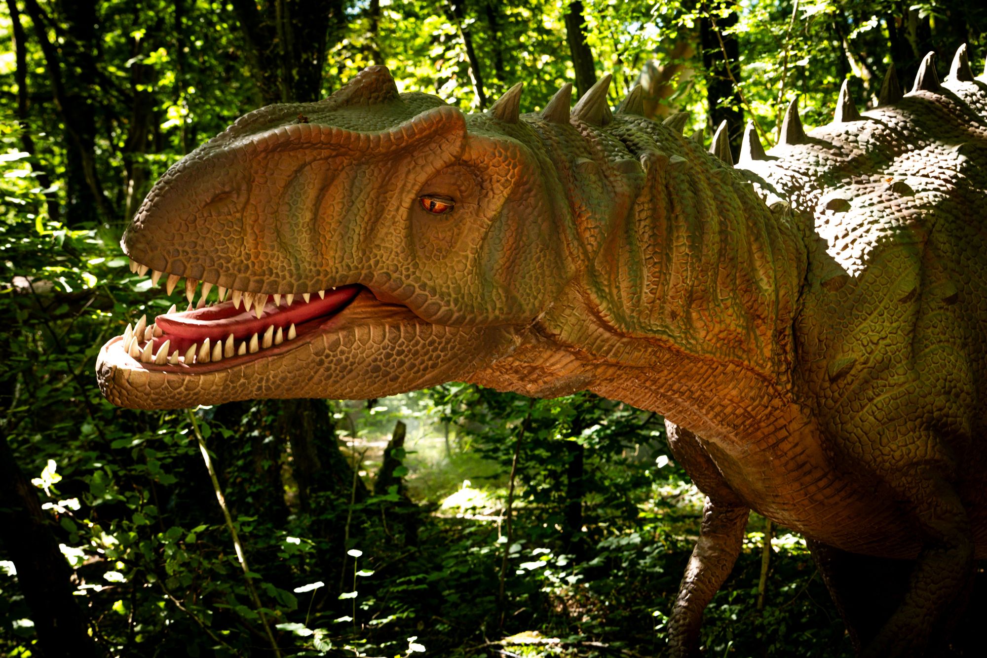 Figura animatrónica de dinosaurio a tamaño real entre los árboles de un bosque