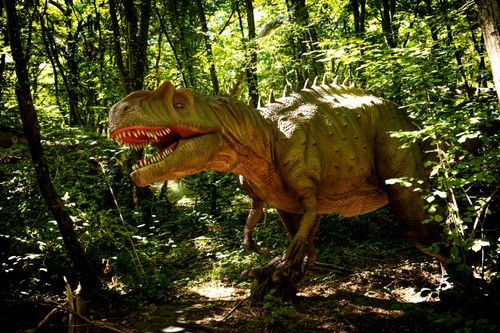 Free A detailed dinosaur sculpture among lush green trees in daylight. Stock Photo