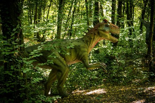 Free A lifelike dinosaur statue positioned in a dense, green forest during the day. Stock Photo