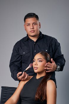 Portrait of a makeup artist applying blush to a model in a studio setting.