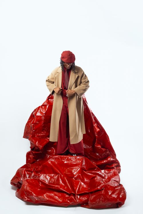 Free Stylish woman in a beige coat and red outfit standing amidst red fabric in a studio setting. Stock Photo