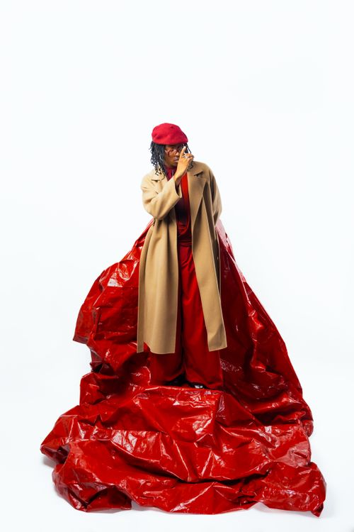 Free Stylish woman in a beige coat stands amidst vibrant red background, exuding elegance. Stock Photo