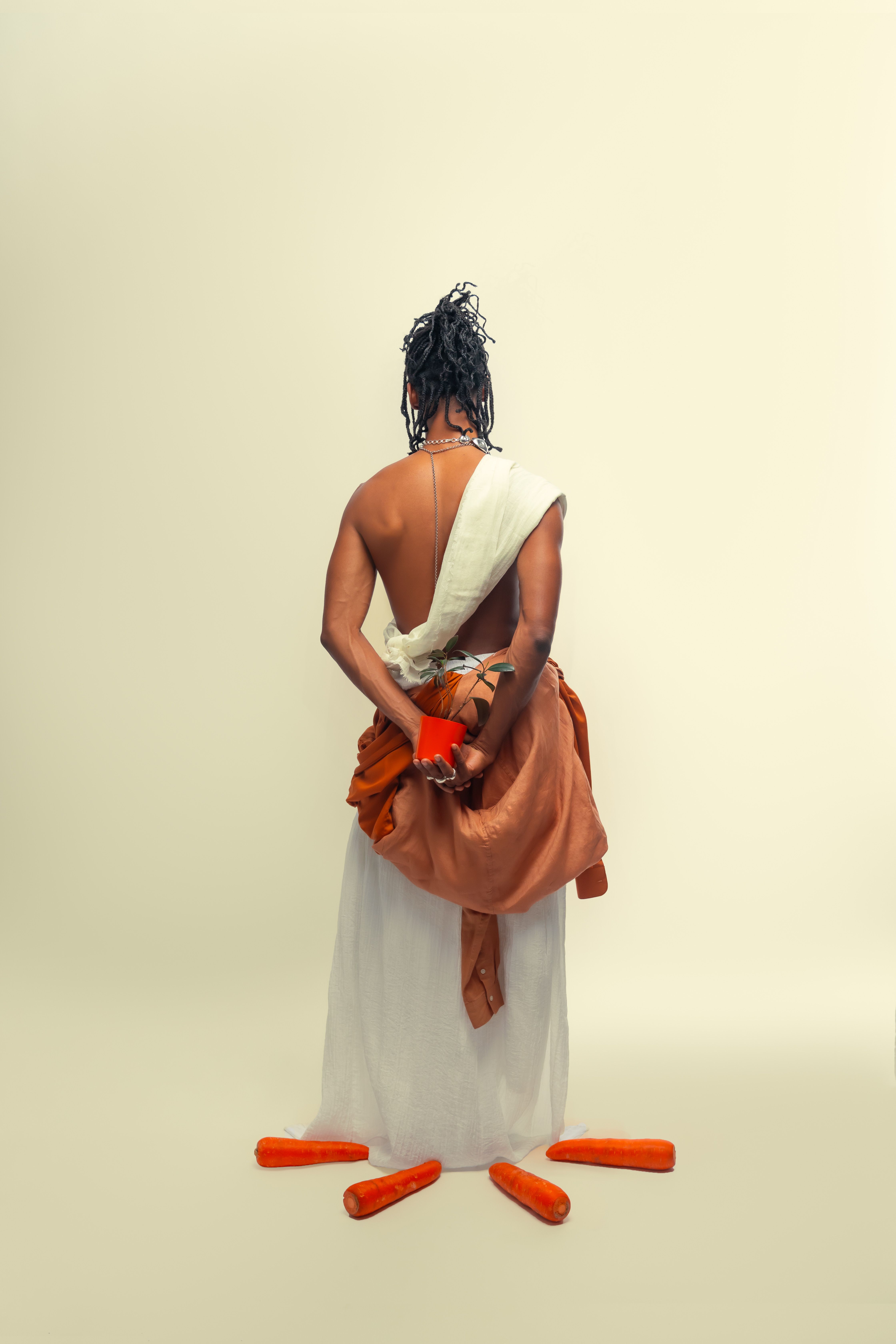 A woman in traditional attire holding a carrot stands gracefully with a minimal background.