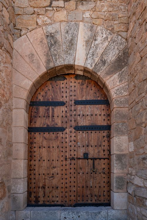Free A rustic wooden door set in a historic stone wall in Villena, Spain. Stock Photo
