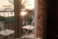 A tranquil sunrise view from a bedroom, overlooking a balcony with palm trees and ocean.