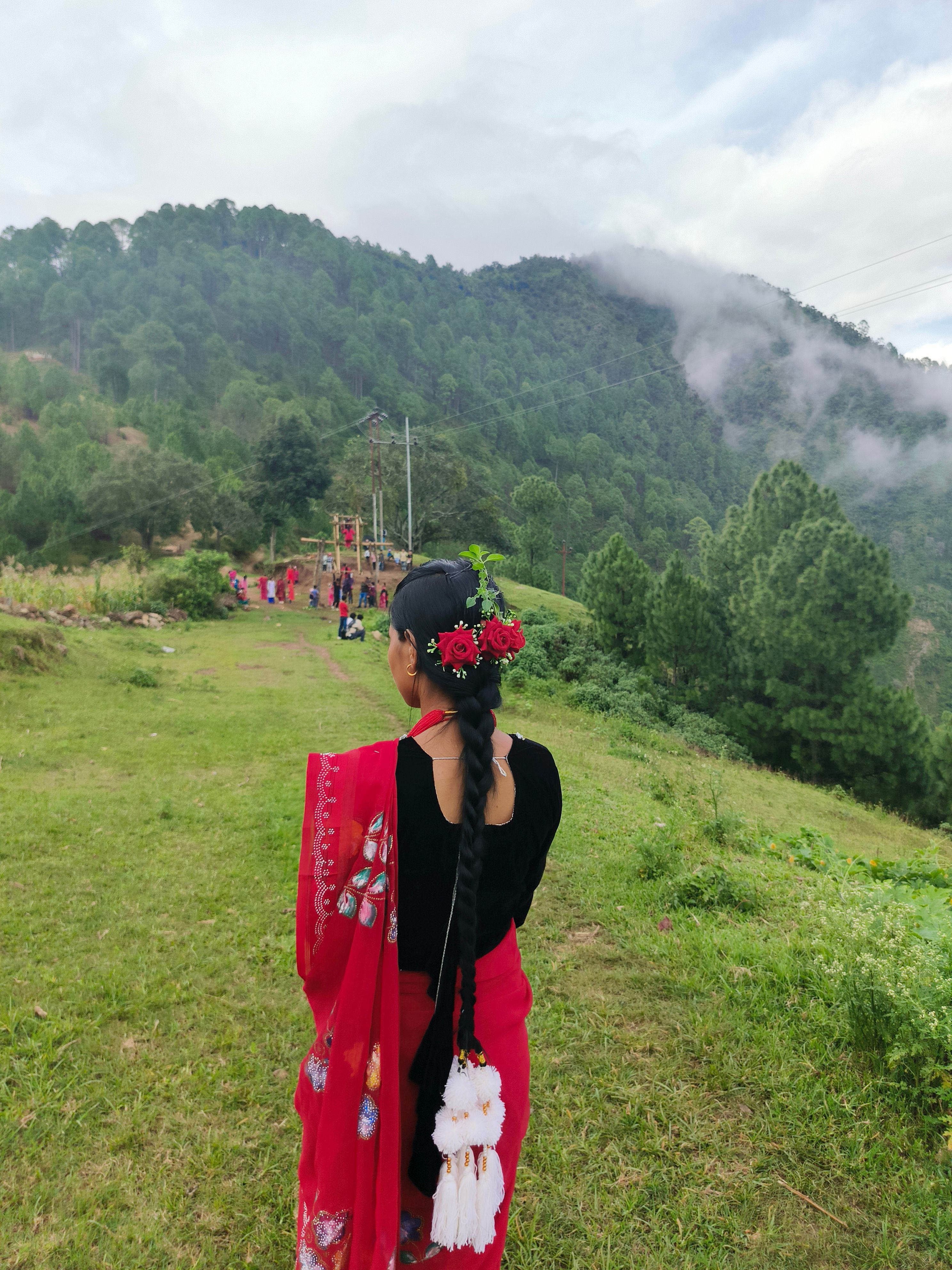 A woman in colorful traditional attire stands amidst lush green hills and misty mountains.