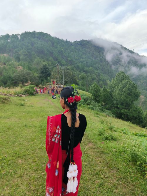 Free A woman in colorful traditional attire stands amidst lush green hills and misty mountains. Stock Photo