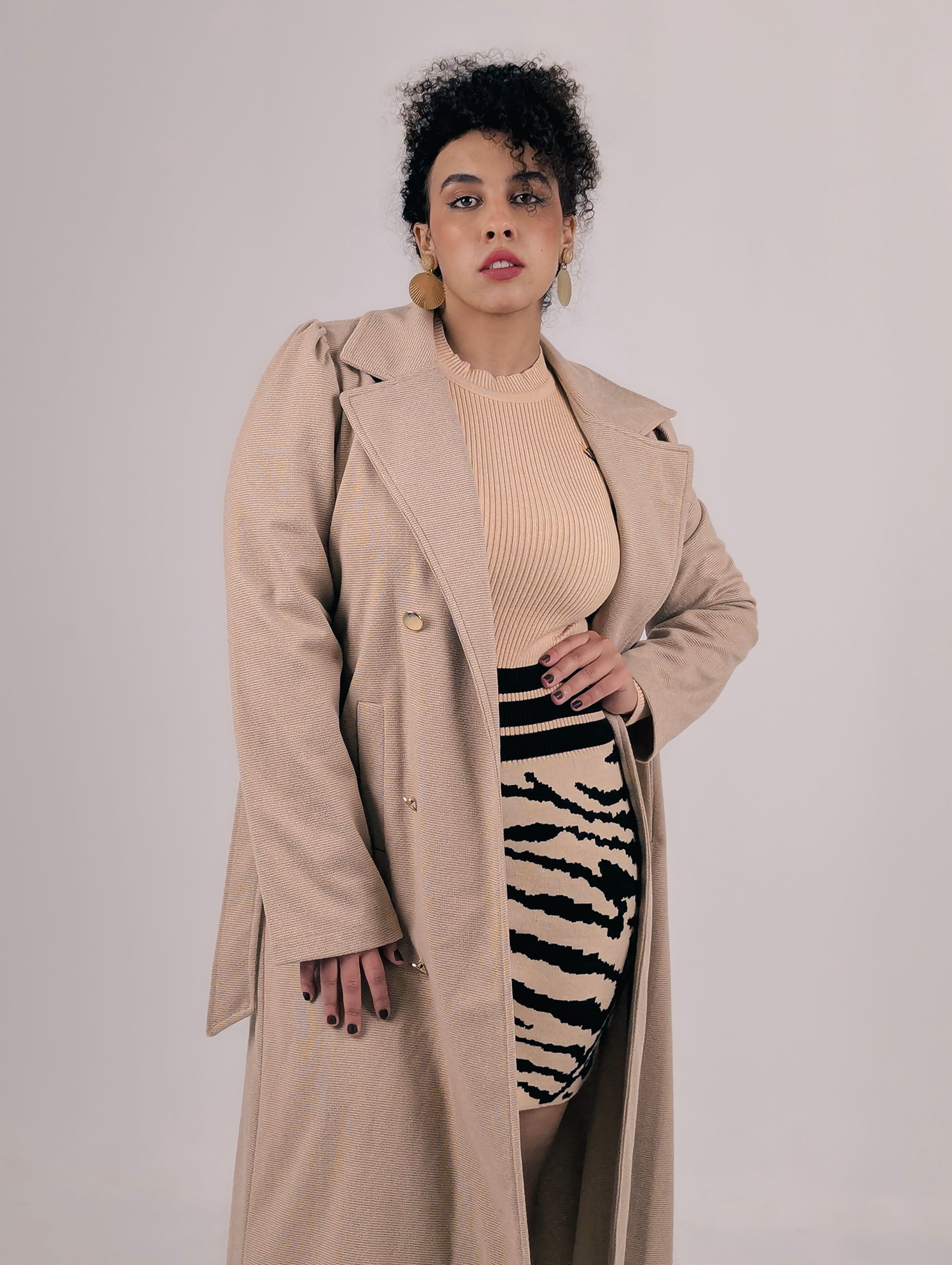 Retrato estiloso de uma jovem mulher com um casaco bege e uma saia com padrão de zebra em cores neutras, exalando elegância e confiança.