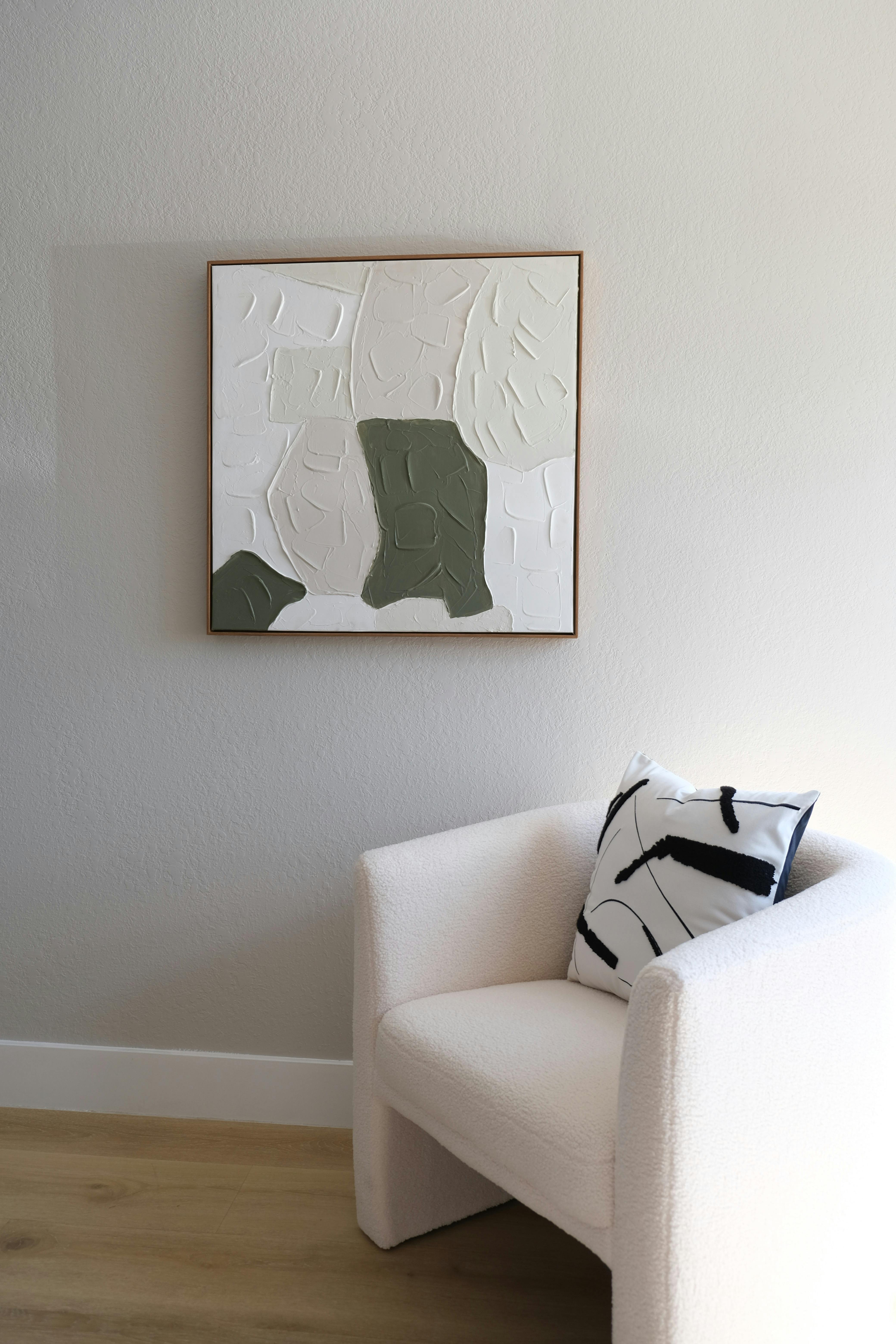 Elegant minimalist interior featuring a textured abstract painting and cozy white armchair.