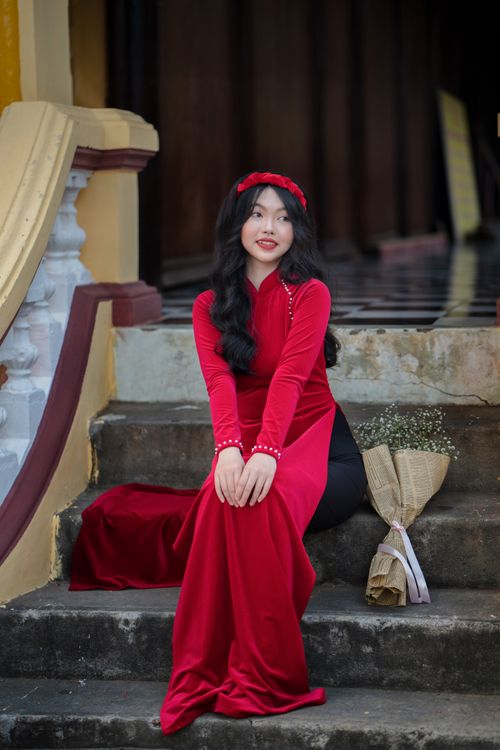 Free Woman in red traditional dress seated on stairs with bouquet. Stock Photo