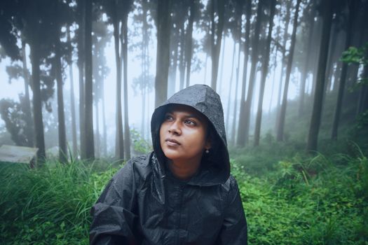 A person in a raincoat surrounded by misty trees in Tukdah, West Bengal, India.