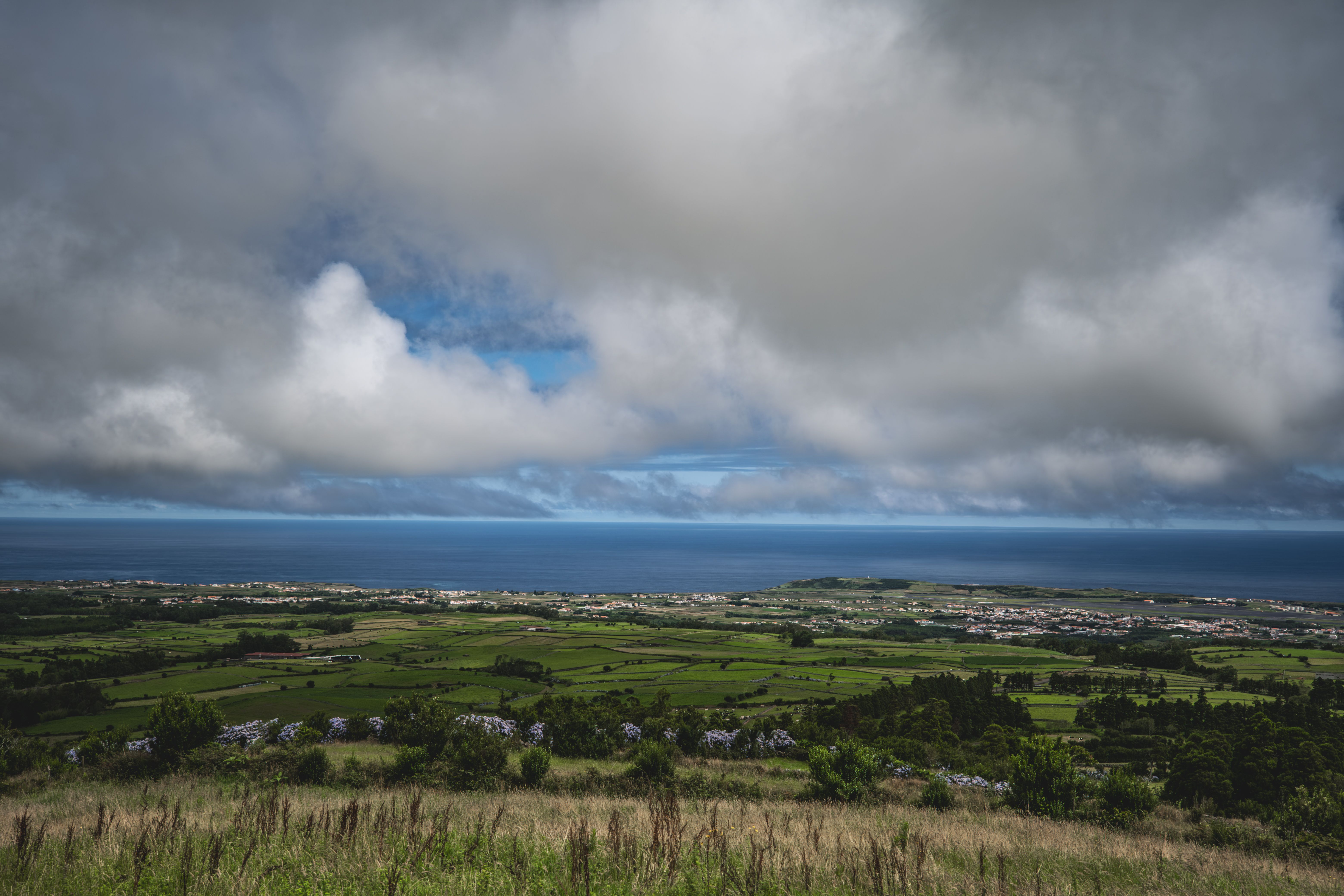 A panoramic shot of a quiet, misty valley in the Azores with green hills and a lone stone house