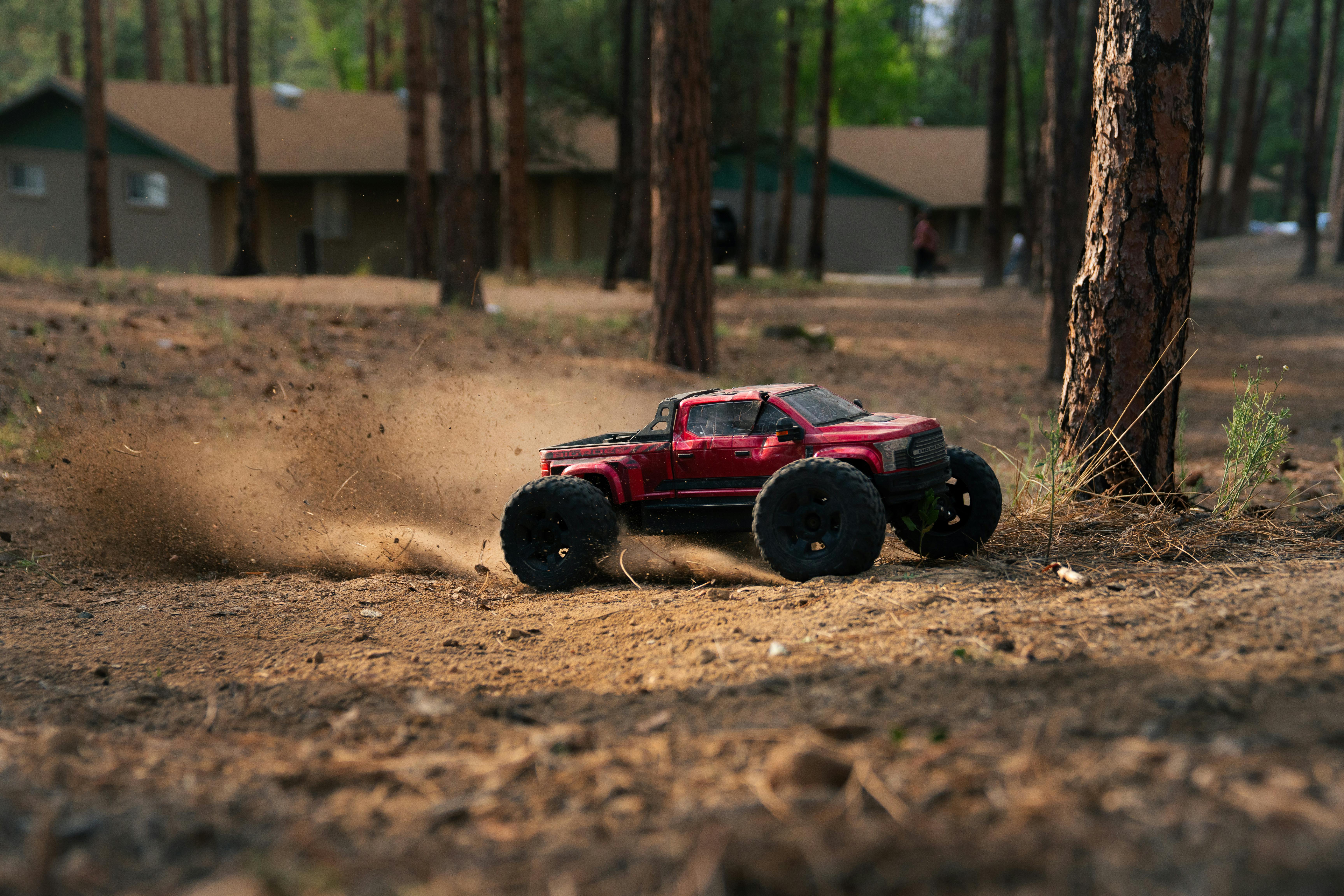 A red remote control truck skids on a forest dirt track, kicking up dust.
