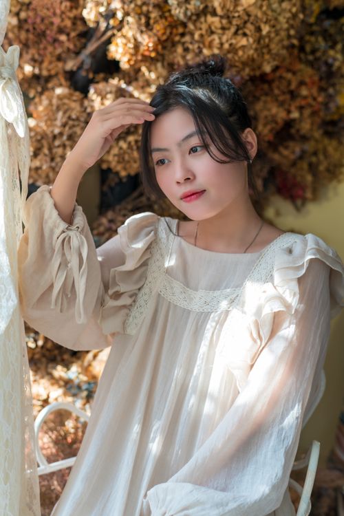 Free A thoughtful woman in a white dress enjoying sunlight in a cozy room. Stock Photo