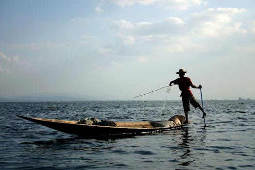 Silhouette of a fisherman balancing on a boat while fishing on Inle Lake, Myanmar.