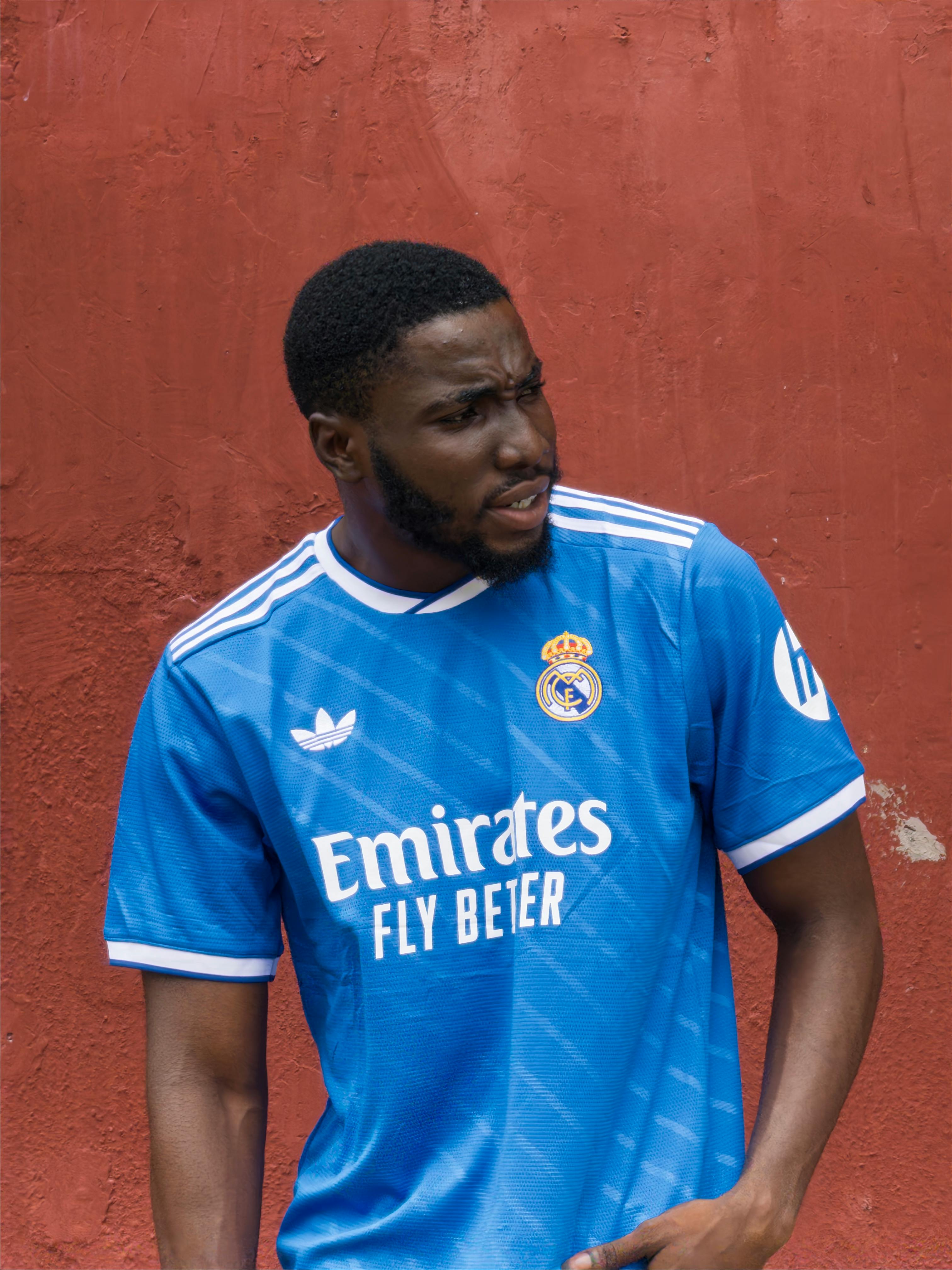Portrait of a young man wearing a blue Real Madrid jersey against a red wall.