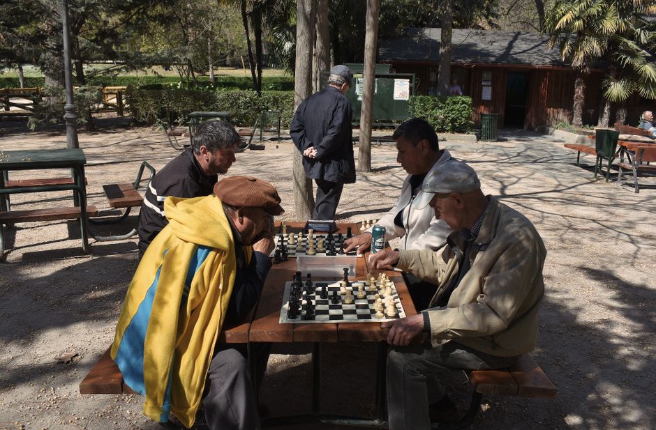 Hombres mayores disfrutando de una partida de ajedrez al aire libre en un soleado parque de Madrid.