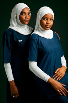 Two young women in medical uniforms and hijabs posing confidently indoors.