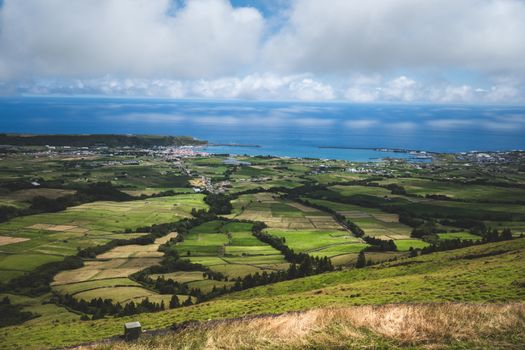 Aerial view of lush green fields stretching to the ocean under a cloudy sky.