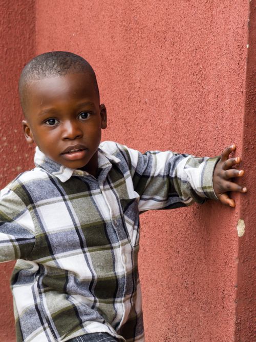 Free A young child leaning against a brick wall outdoors, wearing a plaid shirt and displaying a curious expression. Stock Photo