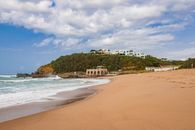 A picturesque beach with hillside architecture under a bright sky, showcasing serene coastal beauty.