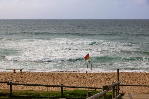 Free A tranquil beach scene with waves, safety flag, and clear sky. Stock Photo