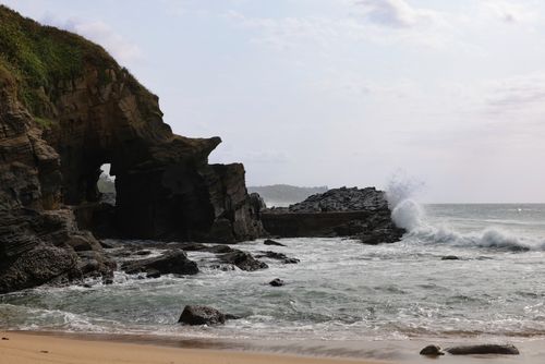 Free Waves crash against rugged cliffs with natural arch, showcasing the wild beauty of the coastline. Stock Photo
