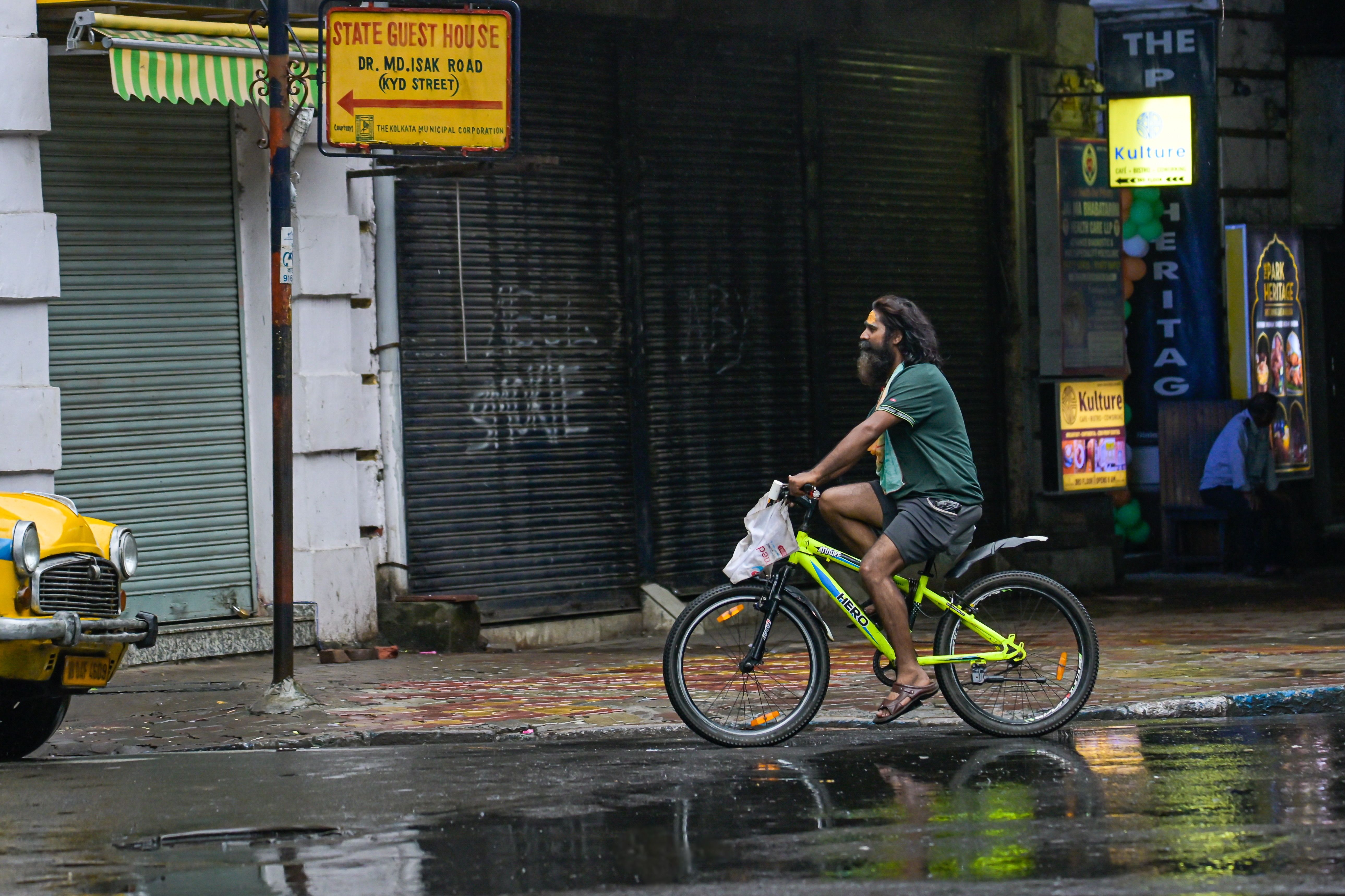 Man riding a bicycle on a wet street in Kolkata after rain, showcasing everyday life and urban scenery.