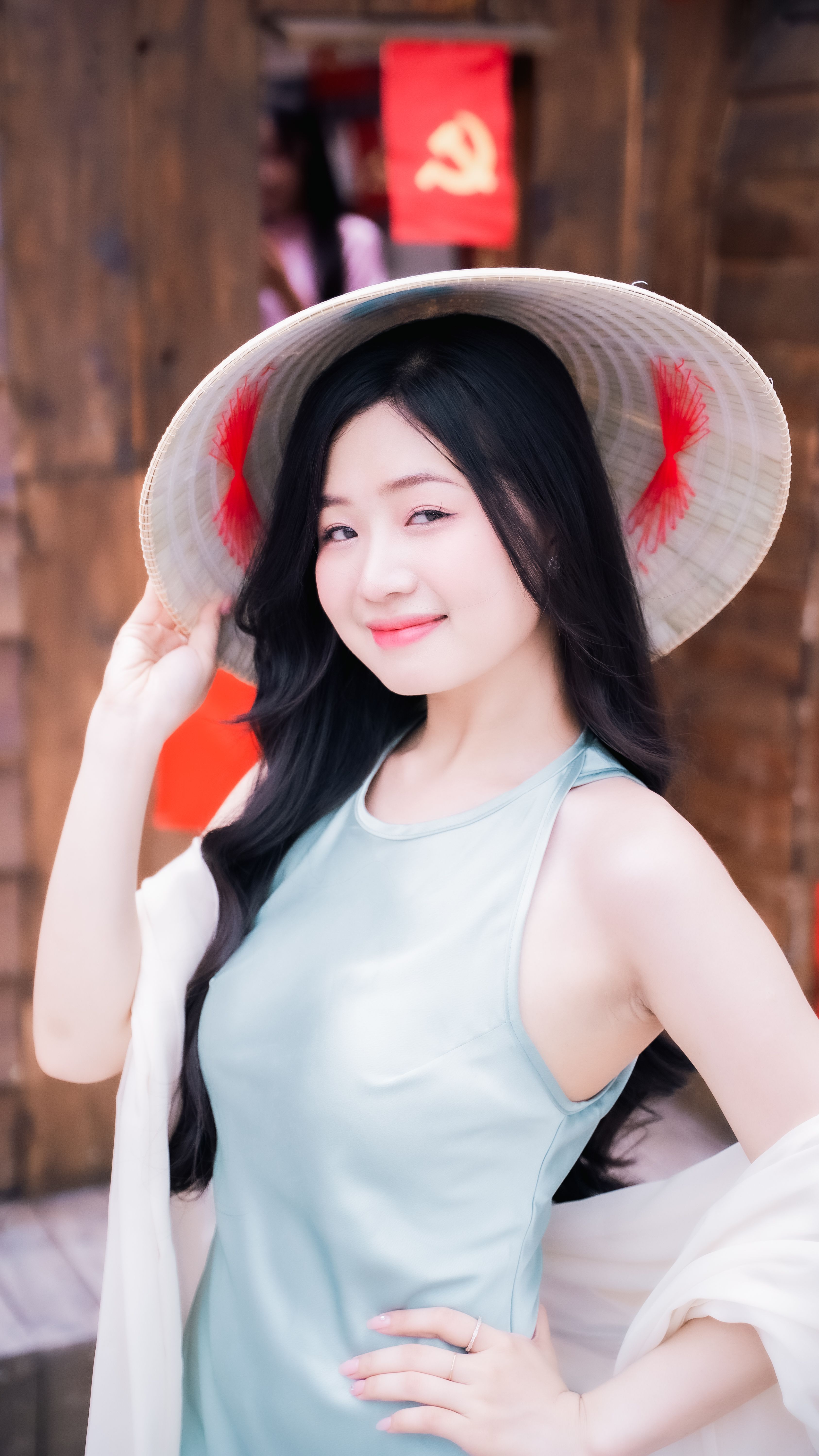 A woman in a blue dress and traditional Asian hat poses confidently outdoors.