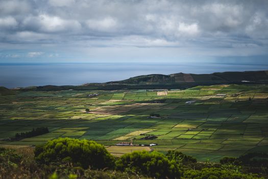 Aerial photo showcasing lush green patchwork fields extending to the ocean under a cloudy sky.