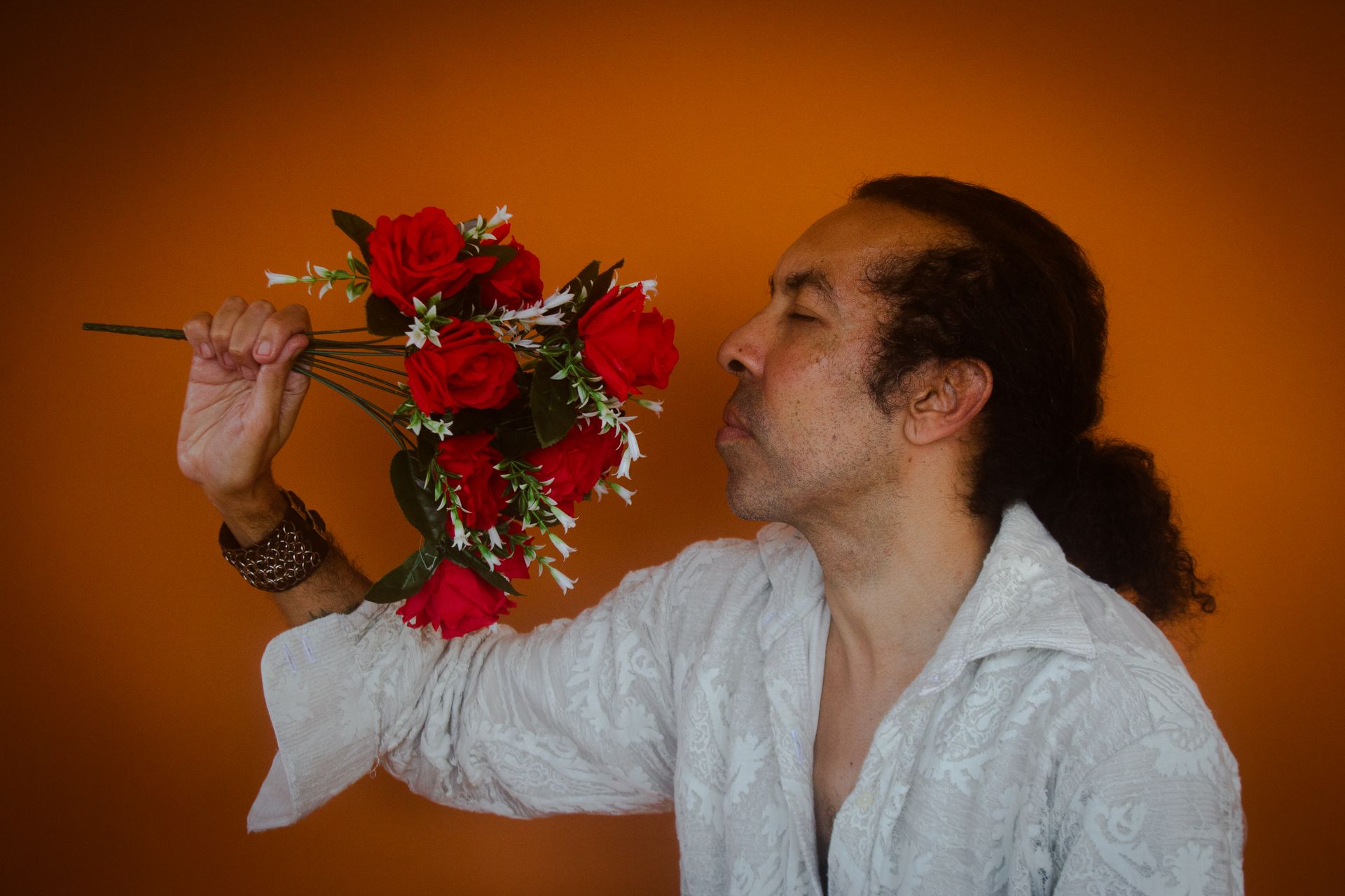 Man relishing the scent of red roses against vibrant orange backdrop in São Paulo studio.