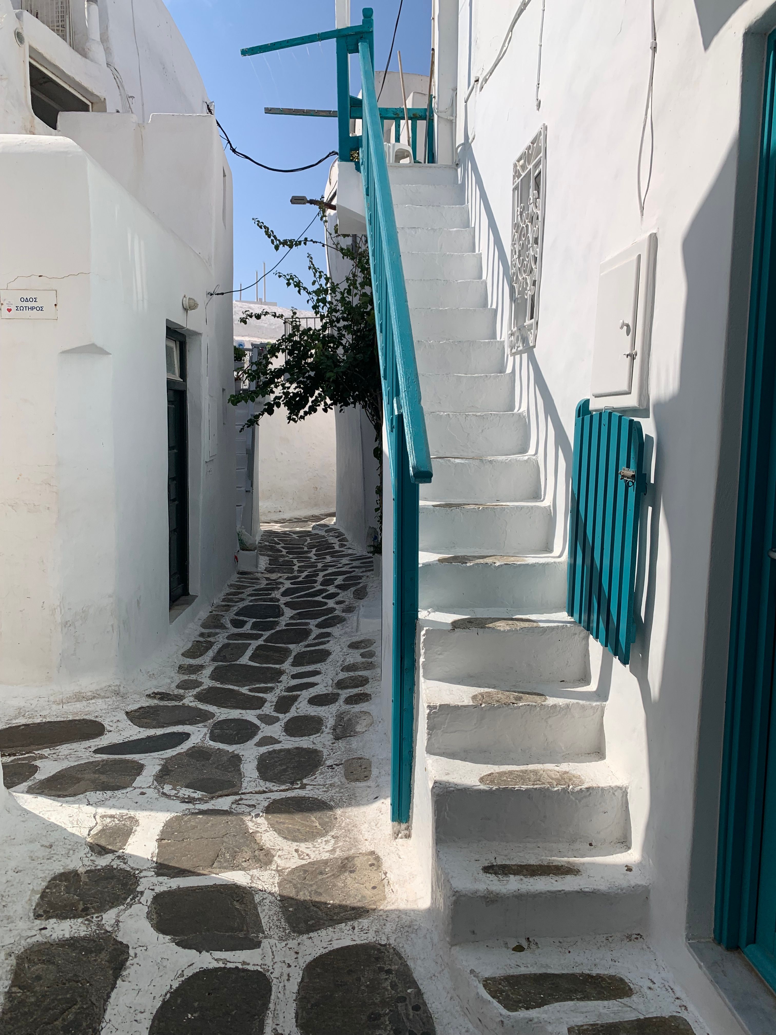 Explore a picturesque whitewashed alley with stone path and teal accents in Mykonos, Greece.
