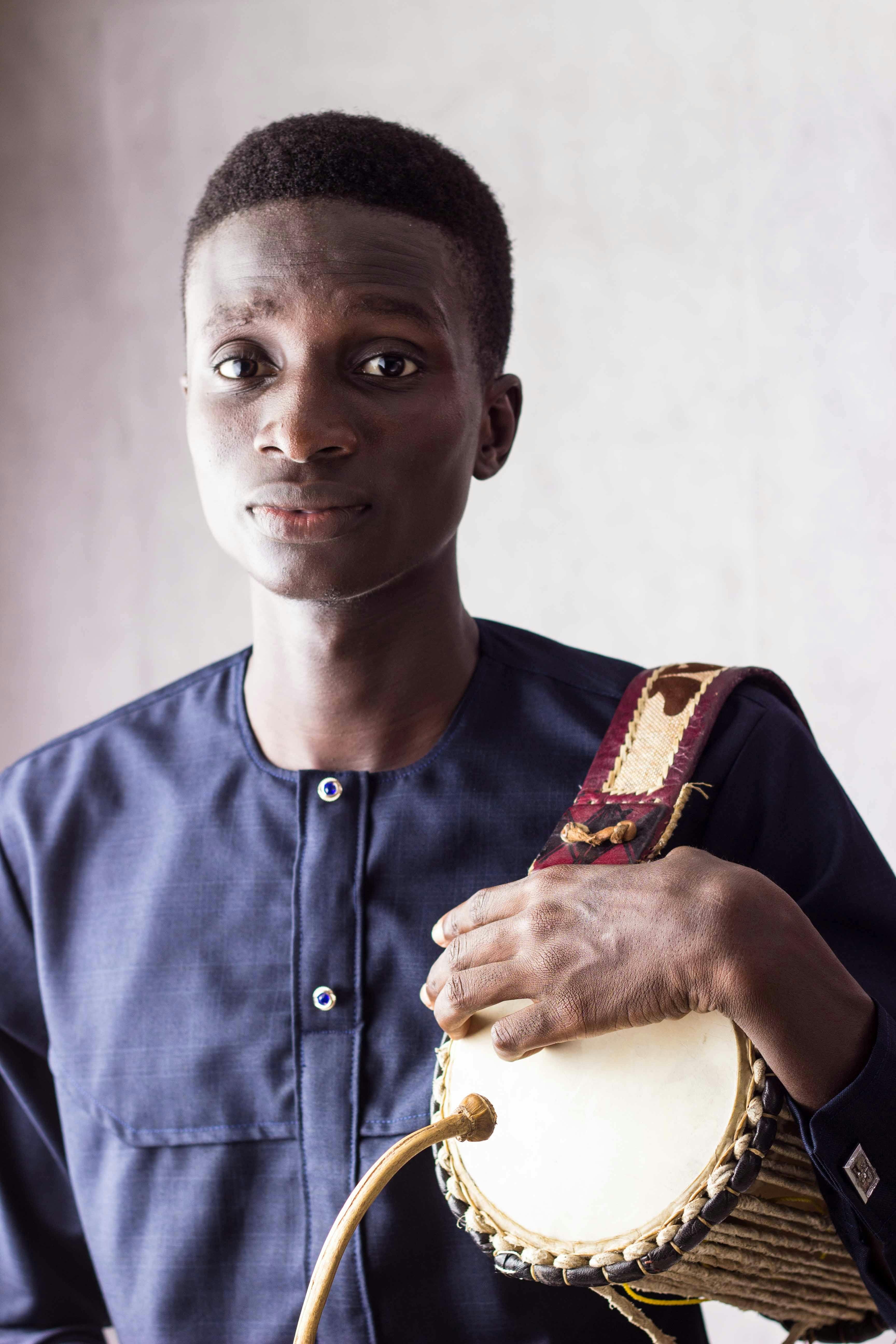 A man holding a traditional drum, showcasing cultural music and fashion.