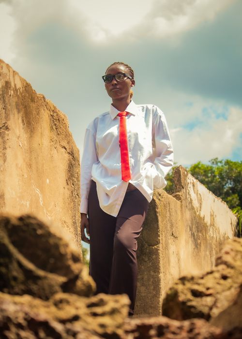 Free Person in tie standing confidently among ruins under a bright sky, showcasing urban fashion. Stock Photo