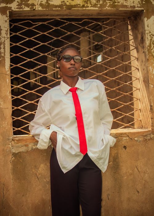 Free A woman with glasses stands confidently in front of a rustic window wearing a red tie and white shirt. Stock Photo