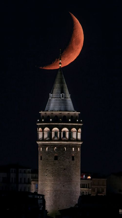 Free Galata Tower illuminated at night with a prominent crescent moon overhead. Stock Photo