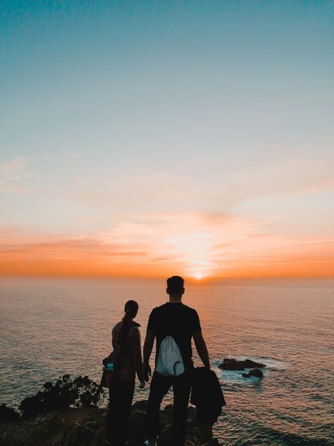 A romantic moment as a couple stands silhouetted, watching the sunset over the Atlantic Ocean in Portugal.