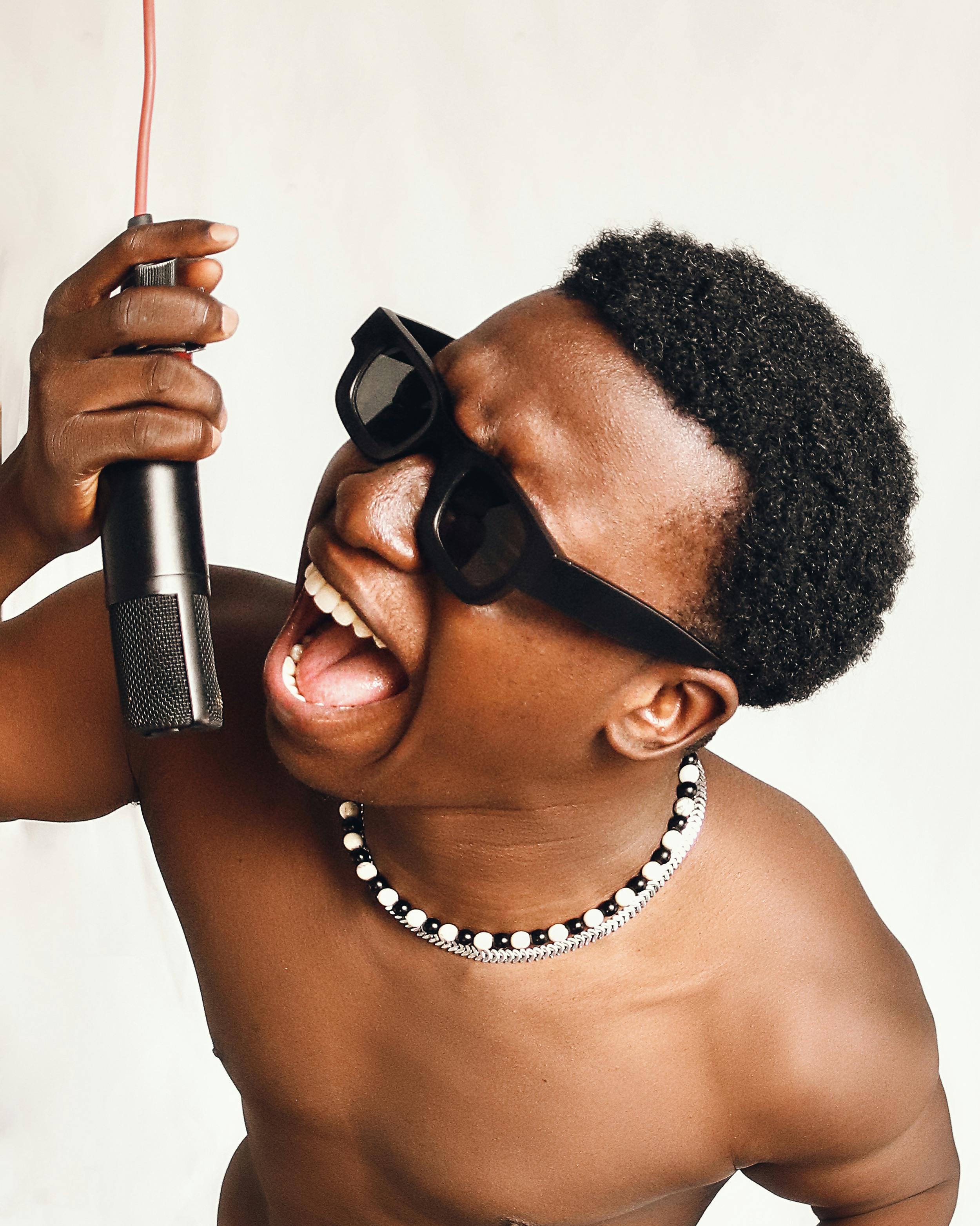 De franc Un jove expressiu cantant a un micròfon, mostrant entusiasme i estil musical amb ulleres de sol. Foto d'estoc