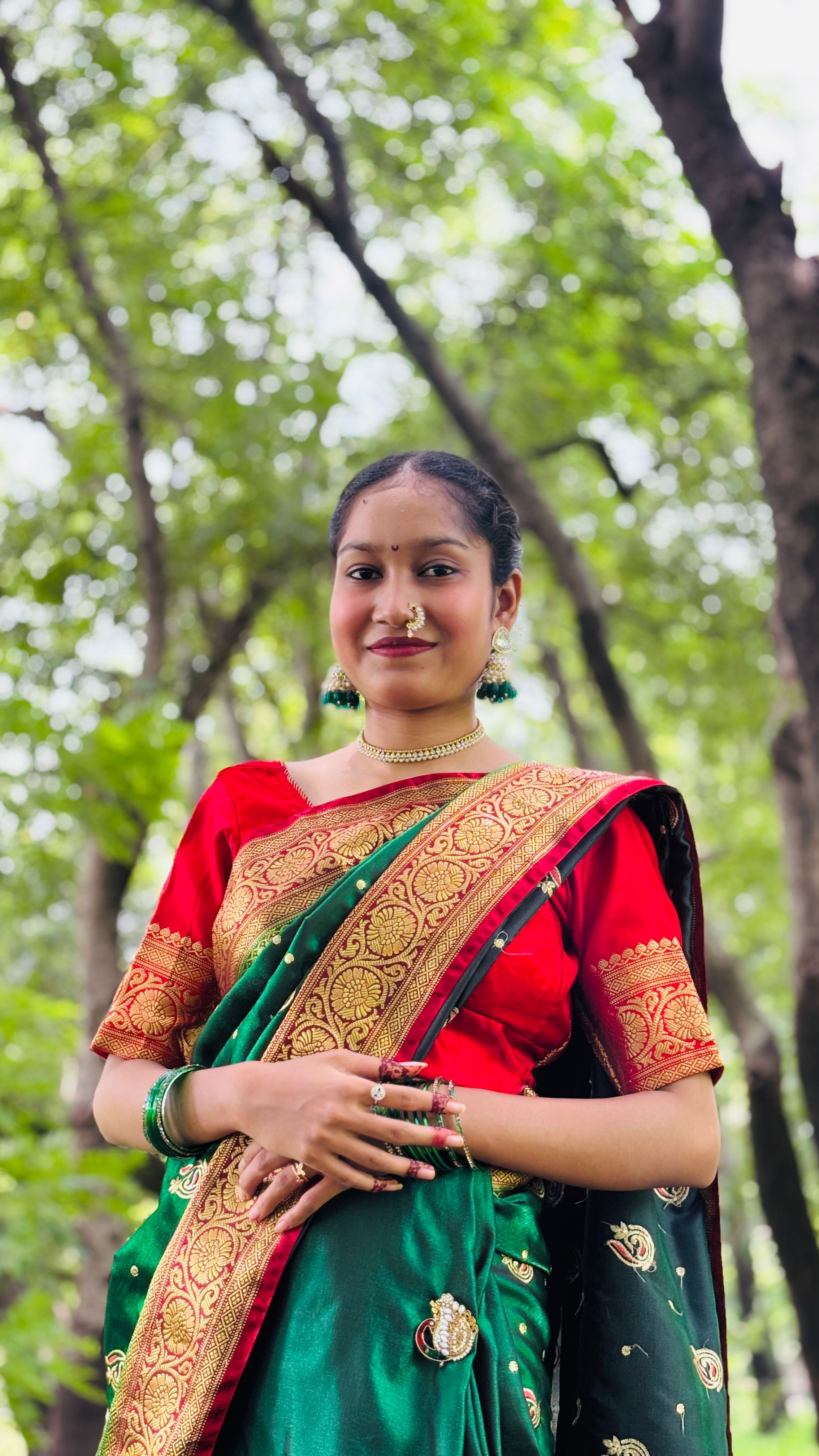 Young woman smiling in a vibrant saree, set against a lush green background, conveying cultural elegance.