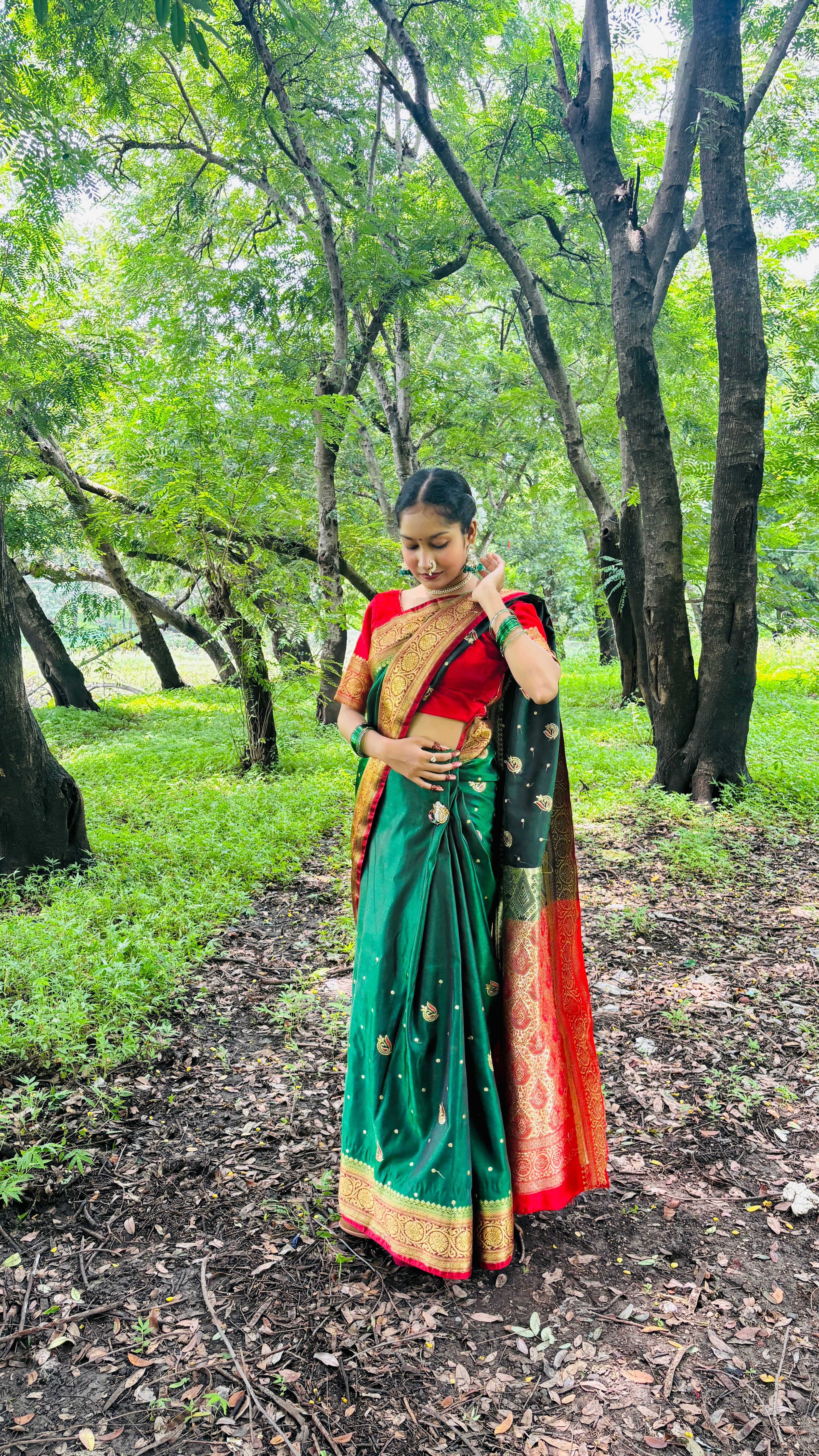 A woman wearing a colorful sari stands in a lush green forest setting.