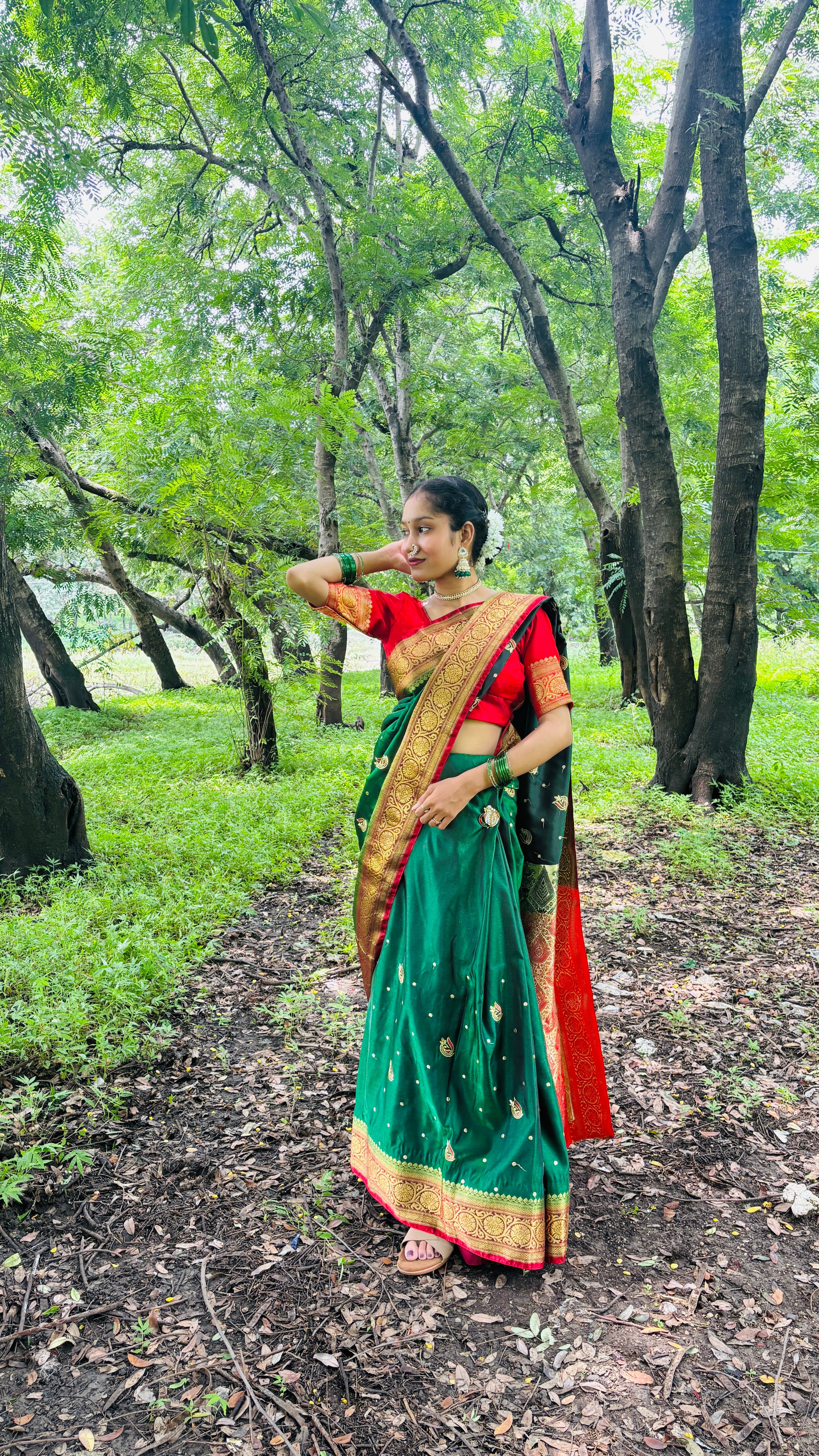 Woman posing in vibrant traditional attire amidst lush greenery in a serene forest.