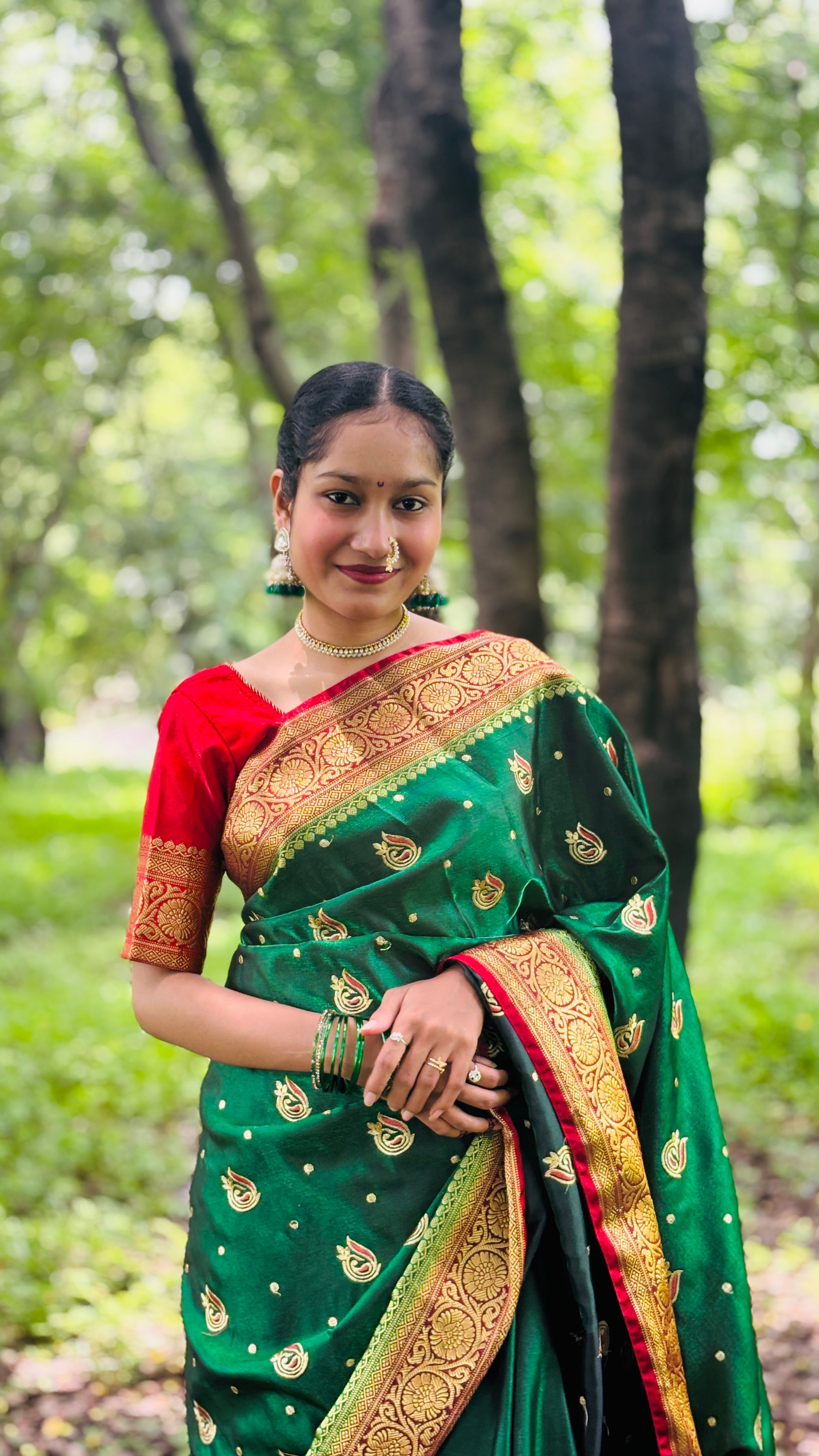 A woman in a traditional green sari posing outdoors in a vibrant forest setting.