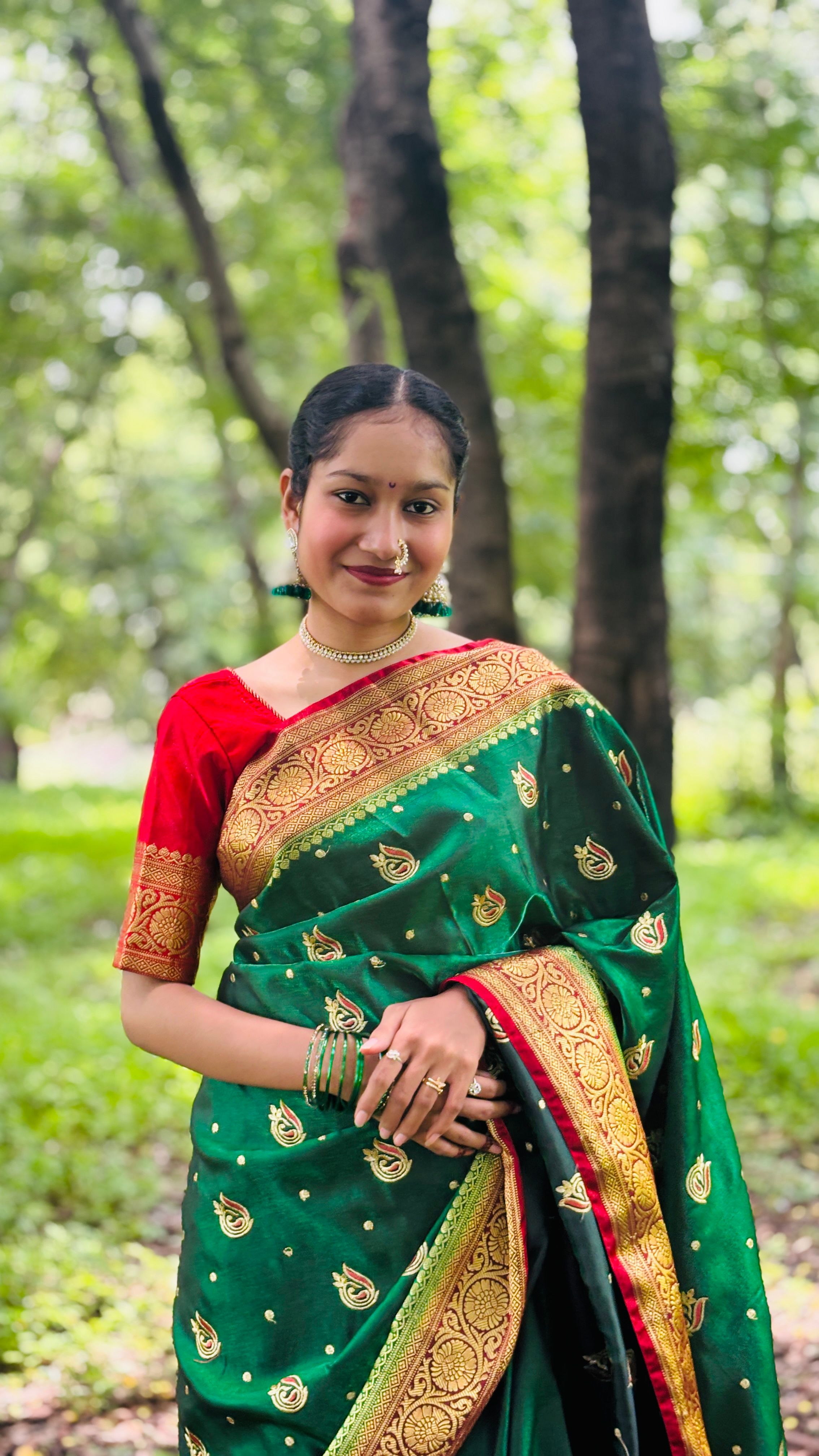 A woman wearing a traditional green saree, standing gracefully in a woodland setting.