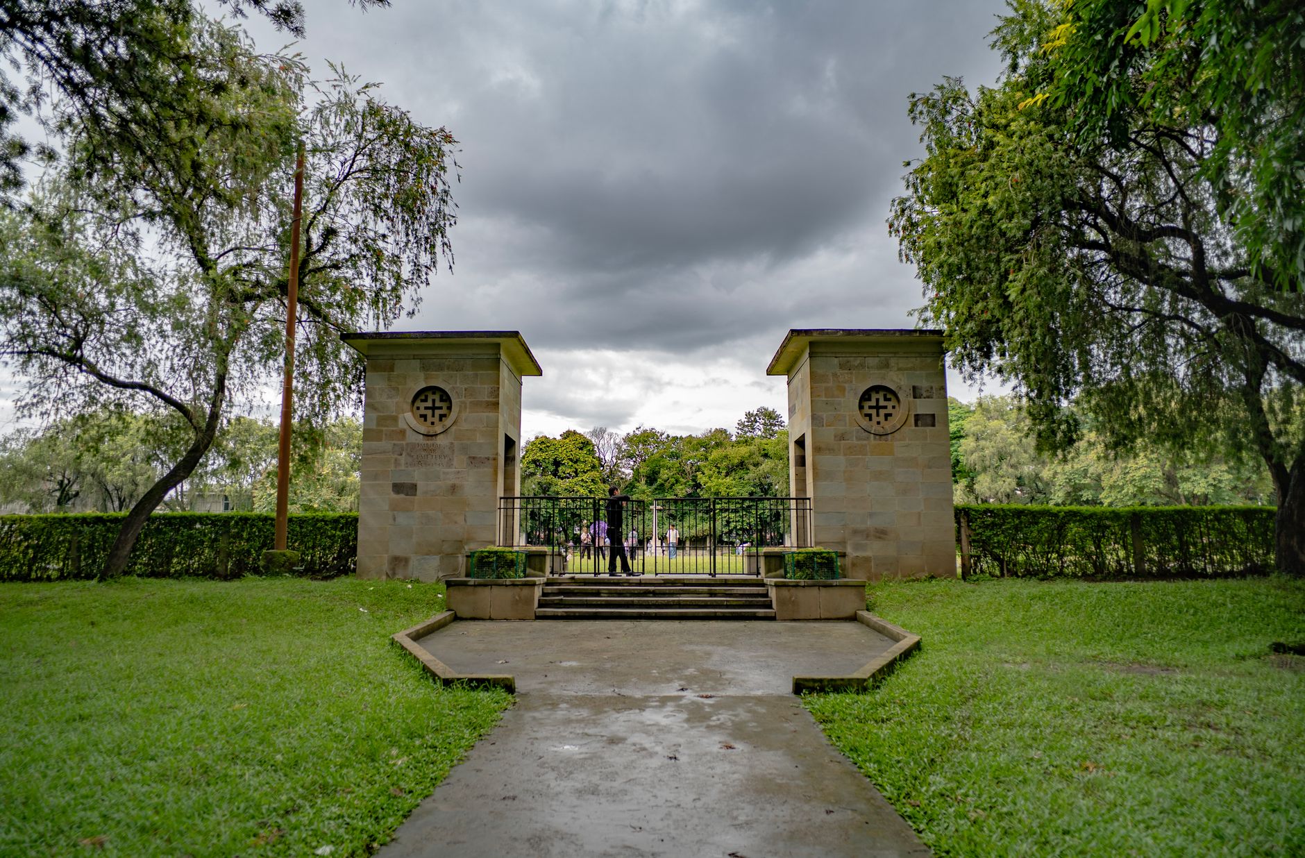Serene view of a World War cemetery entrance in Imphal, India with a dramatic cloudy sky.
