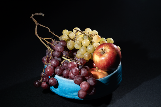 Colorful grapes and apple in a blue bowl on a black backdrop, perfect for food photography.