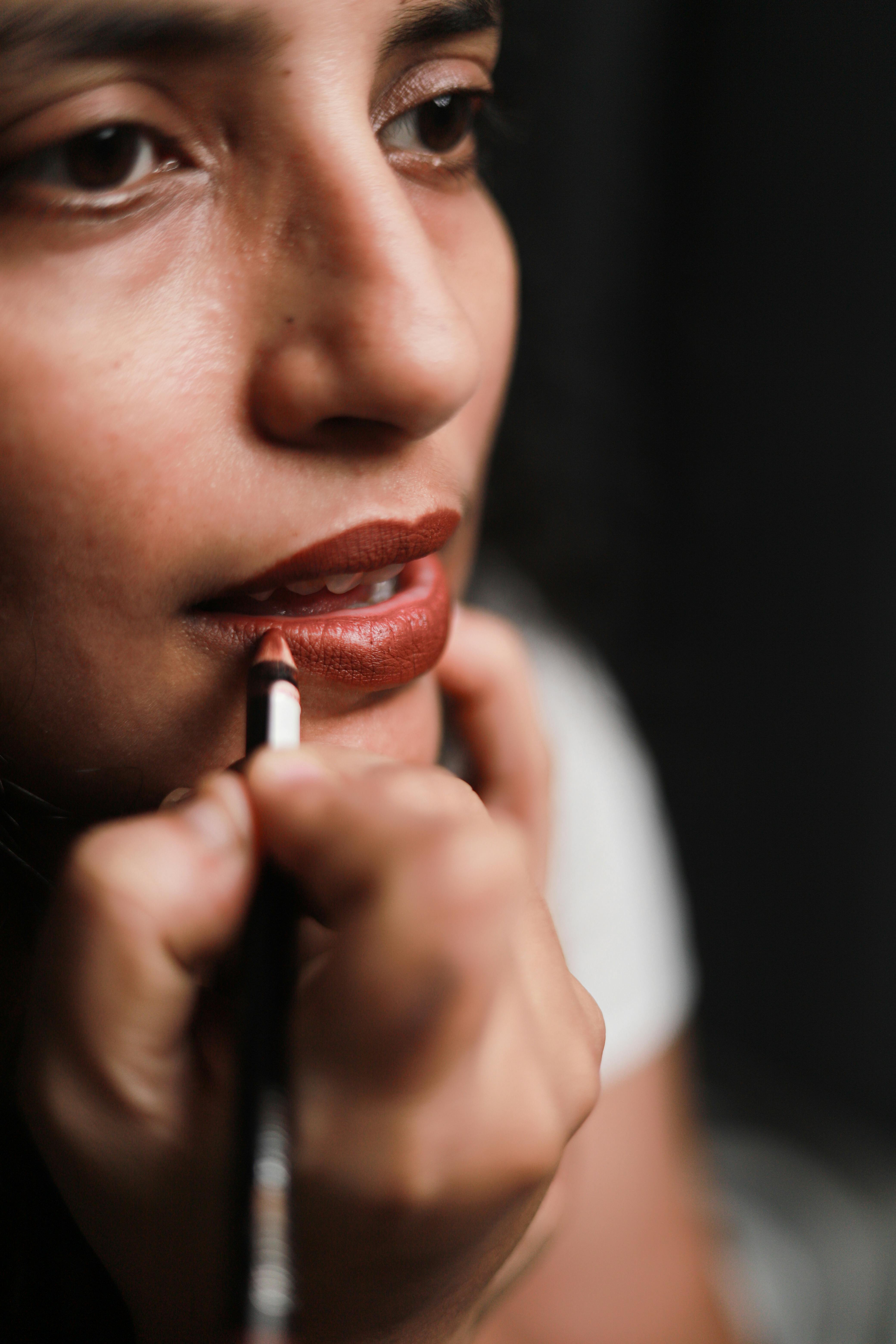 Detailed shot of a woman applying brown lipstick, highlighting makeup artistry.