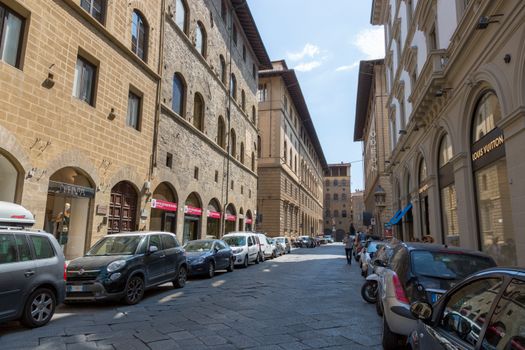 A bustling street scene in Florence featuring classic architecture and boutiques under a clear sky.