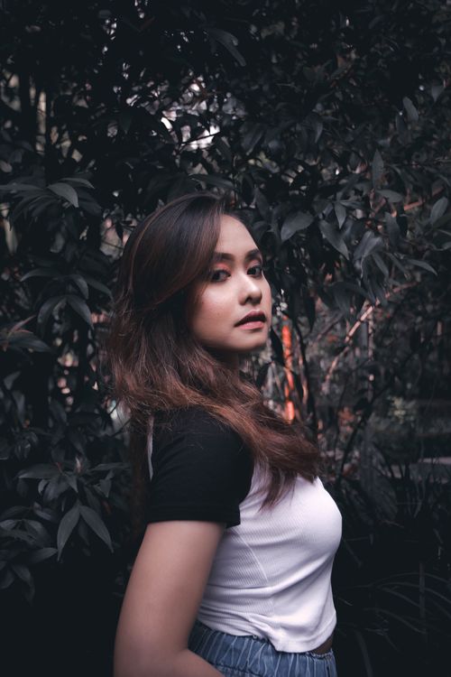 Free A stylish woman posing outdoors amidst lush green foliage. Stock Photo