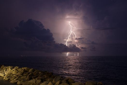Stunning lightning storm over the ocean horizon, captured at night with rocky foreground.