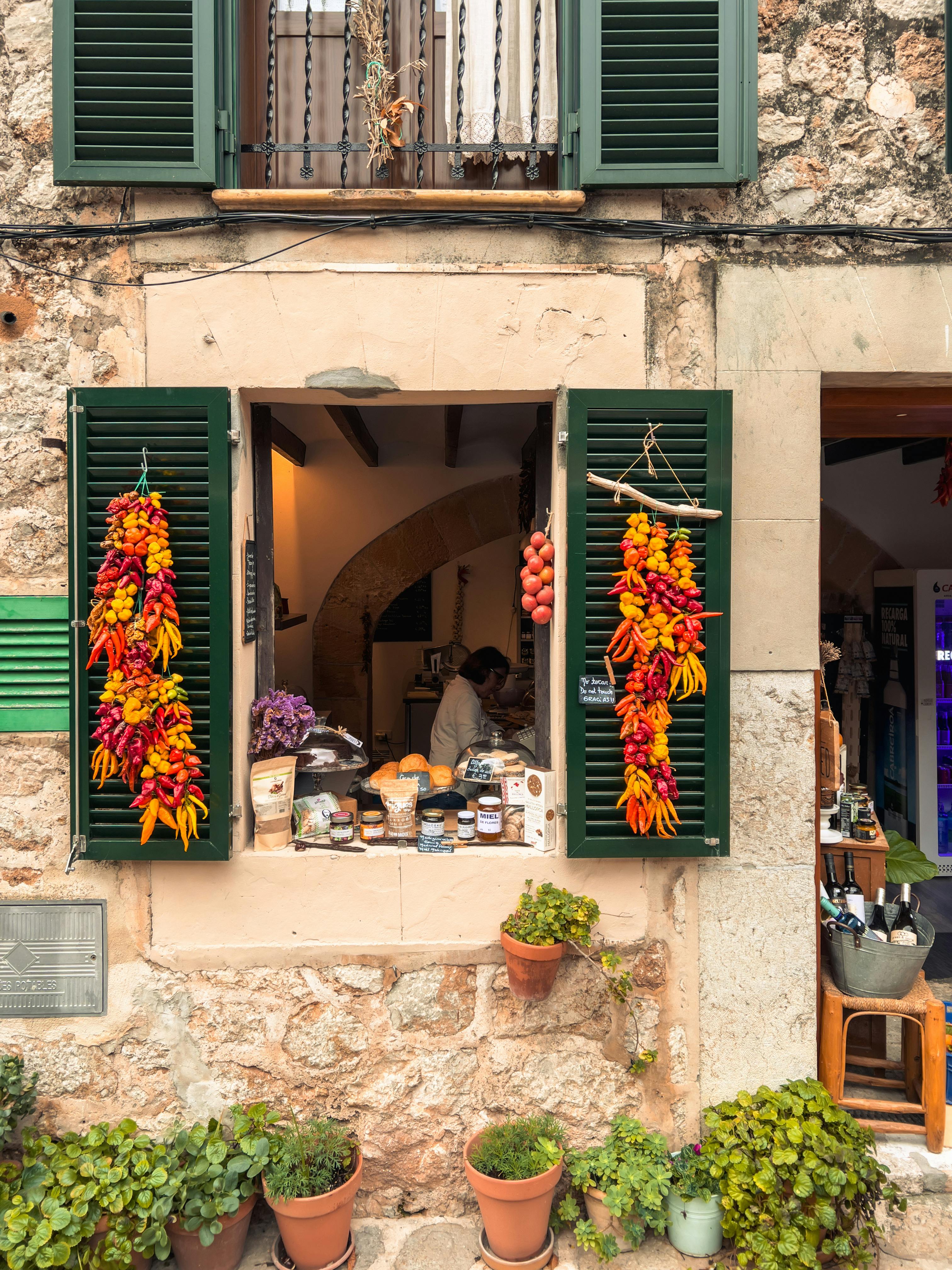 Charming Mediterranean shop window with hanging peppers, jars, and potted plants.